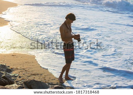 Young man in swimming trunks photographing the sea at sunset on the beach of Ikaria, Greece.
