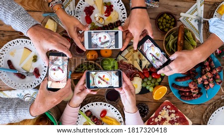 People eating together taking food picture with smartphone to share on social media - concept of celebration - wooden table and mixed food in background