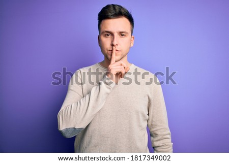 Young handsome caucasian man wearing casual sweater over purple isolated background asking to be quiet with finger on lips. Silence and secret concept.