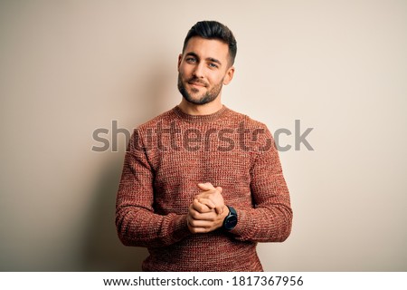 Young handsome man wearing casual sweater standing over isolated white background with hands together and crossed fingers smiling relaxed and cheerful. Success and optimistic