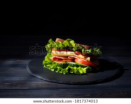 Sandwich with lettuce, tomatoes, cucumbers, ham and cheese on a black stone plate. Dark wooden background. Copy space.  Royalty-Free Stock Photo #1817374013
