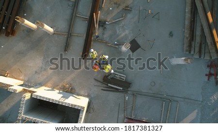 Aerial Top Down Shot of a Constructions Site with Diverse Team of Engineers and Worker with Theodolite Looking Up and Smiling. Heavy Machinery and Construction Workers are Working in the Area.