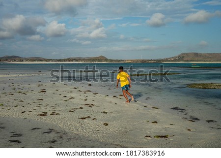 Back view full body portrait of runner jogging on the beach. young man jogging on the beach in summer. Indonesian teenager in shorts and a yellow T-shirt running on the beach