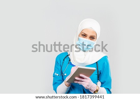 Portrait of friendly muslim doctor or nurse wearing hijab and medical face mask with stethoscope writing prescription to patient on gray background.