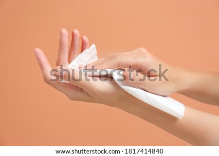 Woman cleaning hands with paper tissue on light brown background, closeup Royalty-Free Stock Photo #1817414840