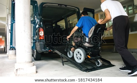 Man on wheelchair using accessible vehicle with ramp for transportation with driver helping. Royalty-Free Stock Photo #1817434184