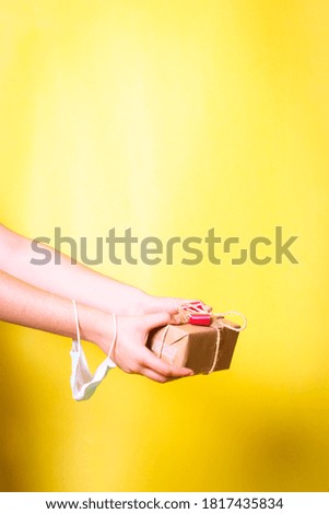 Girl holding a christmas gift box with her hands, with a medical mask on her wrist.