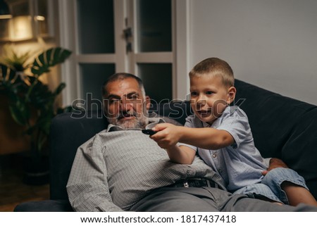 grandfather and grandson laying on the sofa and watching tv at home