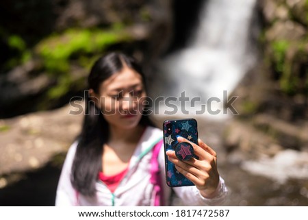 A chinese woman taking a selfie with a waterfall background Sheffield Massachusetts, new england.  