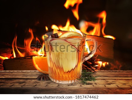 Mulled wine in glass cup on wooden table near fireplace