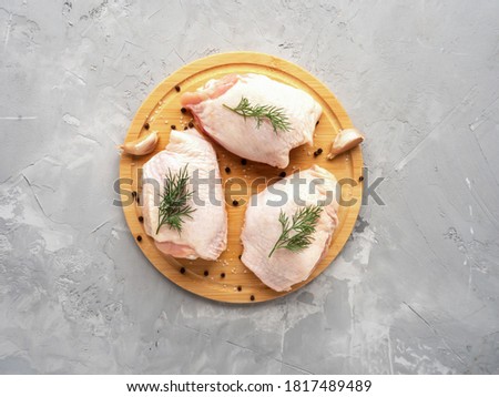 Raw chicken thighs on cutting board with ingredients for cooking at grey concrete kitchen table. Top view with copy space. Royalty-Free Stock Photo #1817489489