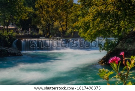 View of flowing Manavgat Waterfall in Antalya, Turkey, with green trees around, on cloudy blue sky background. July 2020, long exposure picture
