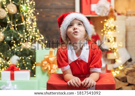 Child with a Christmas present on wooden house background. Happy child with Christmas gift. Portrait of Santa kid with gift looking at camera