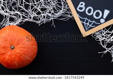 Orange and black Halloween flatlay. Chalk inscription BOO, pumpkin and spider web on black wooden background. Copy space