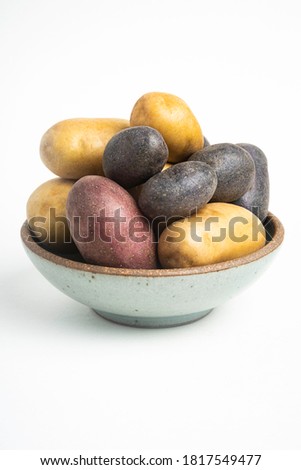 An assorted color raw and fresh potatoes artfully arranged on a bowl and set on white background.
