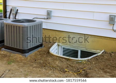 Air conditioning system assembled on performing preventive maintenance in a window well for basement construction new residential home Royalty-Free Stock Photo #1817559566