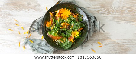 flat lay bowl of vegetarian salad with arugula and orange and edible marigold flowers on light table
