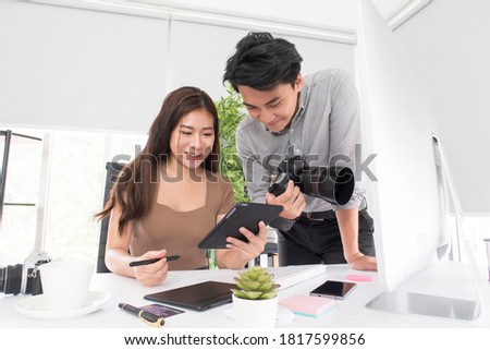Happy young Asian man professional photographer and woman graphic designer checking a picture on a tablet while working together in the modern office. Business Creative people, Teamwork concept.