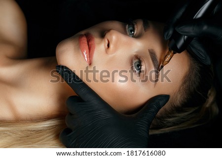 Beautician hand doing eyebrow permanent makeup on a pretty woman face
 Royalty-Free Stock Photo #1817616080
