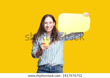 happy joyful young woman in casual holding yellow smartphone and blank speech bubble
