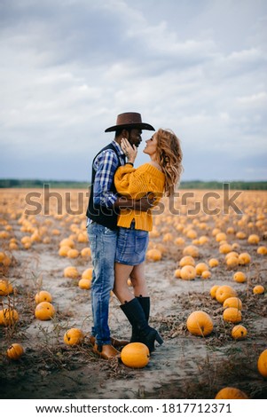 Happy interracial couple in love stands in a pumpkin field. Thanksgiving day concept. Wide shot.