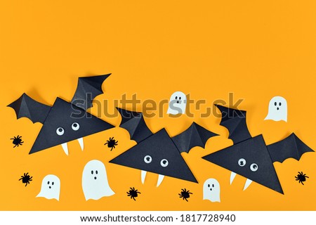 Cute paper vampire bats with googly eyes and ghosts and spiders on orange Halloween background with empty copy space
