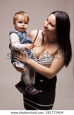 Cute happy baby girl posing with her mother on gray isolated background