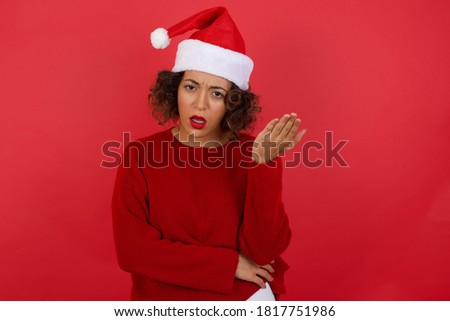 What the hell are you talking about, nonsense. Studio shot of frustrated woman wearing Christmas hat  gesturing with raised palm, frowning, being displeased and confused with dumb question.