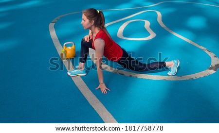 An athlete does a stretch on a street sports field. Young female athlete doing workout, training with a kettlebell in the open air.