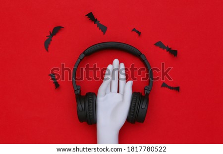 Mannequin hand and stereo headphones with bats on red background
