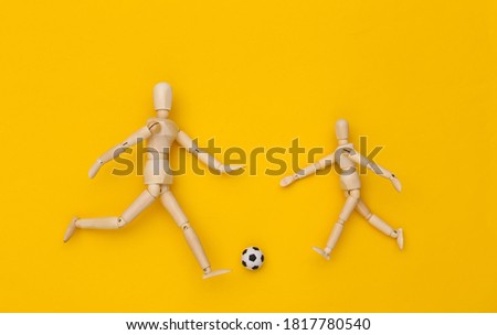 Two wooden puppet playing soccer with a ball on yellow background