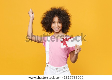Happy little african american kid girl 12-13 years old in pink t-shirt isolated on yellow wall background. Childhood lifestyle concept. 