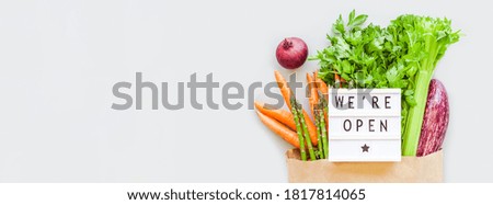 End of quarantine. Fresh organic vegetables in eco craft paper shopping bag with text We're Open lightbox flat lay, top view on gray background. Sustainable lifestyle. Zero waste, plastic free concept