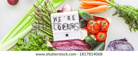 End of quarantine. Fresh organic vegetables in eco friendly wooden box with text We're Open lightbox flat lay, top view on gray background. Sustainable lifestyle. Zero waste, plastic free concept
