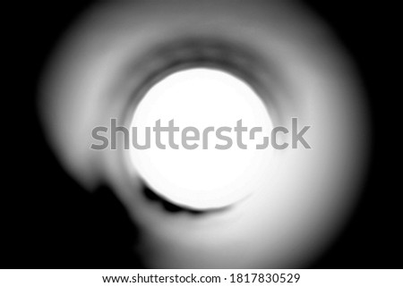 A real blurry photo of a dark round tunnel with a bright light in the end. Round hall with bright light in blur.