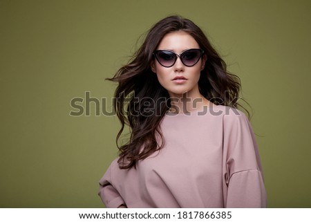 High fashion photo of a beautiful elegant young woman in a pretty pink jumpsuit and sunglasses, posing over green background. Slim figure. Studio Shot. Femininity and tenderness