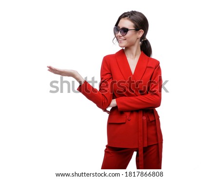 High fashion photo of a beautiful elegant young woman in a pretty red suit, jacket, pants, trousers and sunglasses posing over white background. Slim figure. Studio Shot. Businesswoman