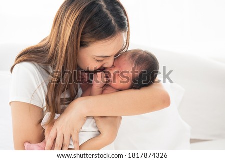 Pretty asian woman smile and holding a newborn baby in her arms. Happy family. Asia mother lifting and kiss her adorable infant baby on white. love people concept