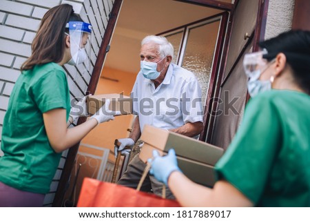 Young female volunteers in mask gives an elderly man boxes with food near his house. Quarantined, isolated. Coronavirus covid-19. Donation Royalty-Free Stock Photo #1817889017