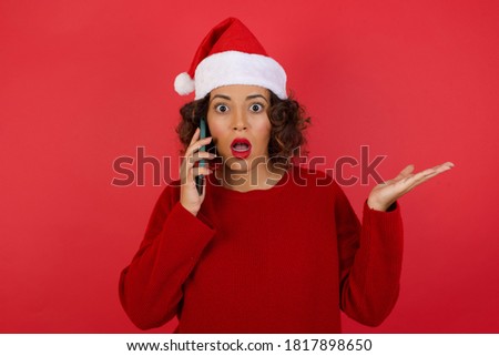 Young woman wearing Christmas hat talking on the phone over isolated background stressed with hand on face, shocked with shame and surprise face, angry and frustrated. Fear and upset for mistake.