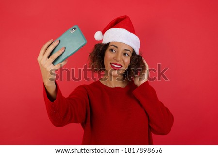 Portrait of a pretty happy woman wearing Christmas hat taking a selfie isolated over bright background