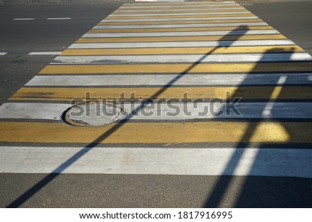 yellow and white pedestrian crossing with a hatch on an asphalt road and a shadow from a traffic light and a road sign