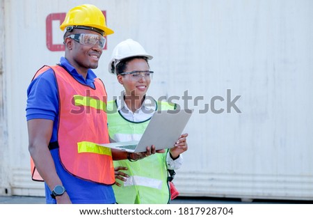African American factory workers man and woman stand and look to right side together in cargo shipping workplace area. Concept of good system and manager support for better industrial business.