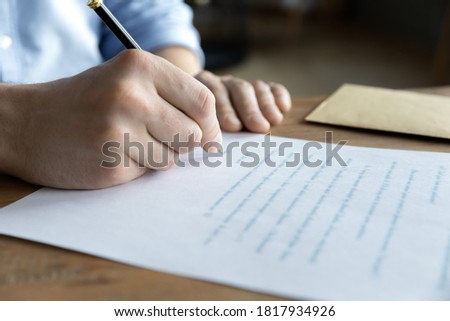 Crop close up of male sit at desk writing paper letter closing deal at workplace. Caucasian man employee or worker sign paperwork document, make agreement with client. Employment concept.