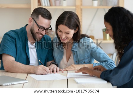 Happy young married couple signing contract, making successful deal, smiling young husband wearing glasses putting signature on legal documents, purchasing new house, taking loan or mortgage