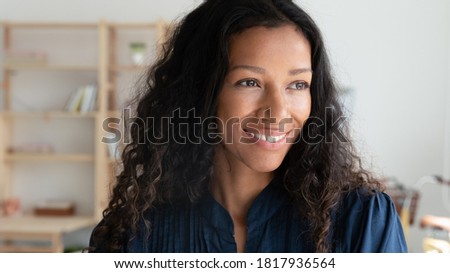 Head shot close up smiling dreamy African American businesswoman dreaming about future, standing in office, motivated happy employee pondering project strategy or startup idea, business vision