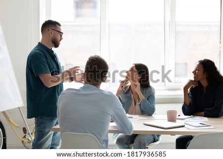 Diverse employees listening to confident coach mentor at meeting, young businessman wearing glasses training staff, making presentation, explaining project strategy at corporate briefing Royalty-Free Stock Photo #1817936585