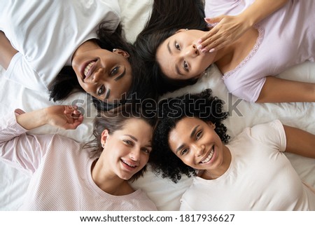 Above top head shot close up view happy attractive young mixed race women best friends lying on bed, having fun enjoying sleepover hen party time together, spending free weekend time indoors. Royalty-Free Stock Photo #1817936627