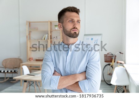 Head shot confident young businessman startup owner pondering strategy close up, standing with arms crossed in modern office, looking to aside, thoughtful employee thinking about new opportunities