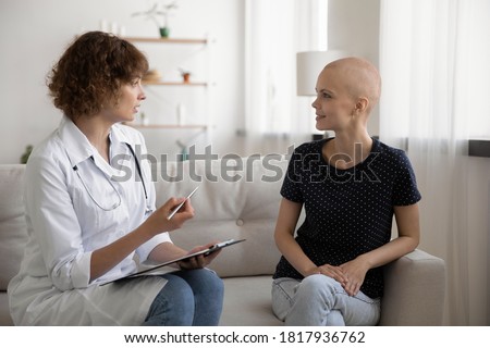 Doctor sit on sofa at home or hospital talk consult young Caucasian hairless sick woman suffer from oncology. Nurse speak with bald female patient struggling with cancer, healthcare. Medicine concept. Royalty-Free Stock Photo #1817936762